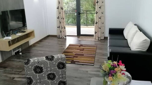 A modern living room with a flat-screen TV, a sofa, a patterned armchair, and a wooden floor. - Bobato Appartement D (Curepipe)
