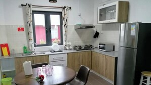 A compact kitchen with a dining area, including a table with chairs, a refrigerator, a microwave, and a sink. - Bobato Appartement D (Curepipe)