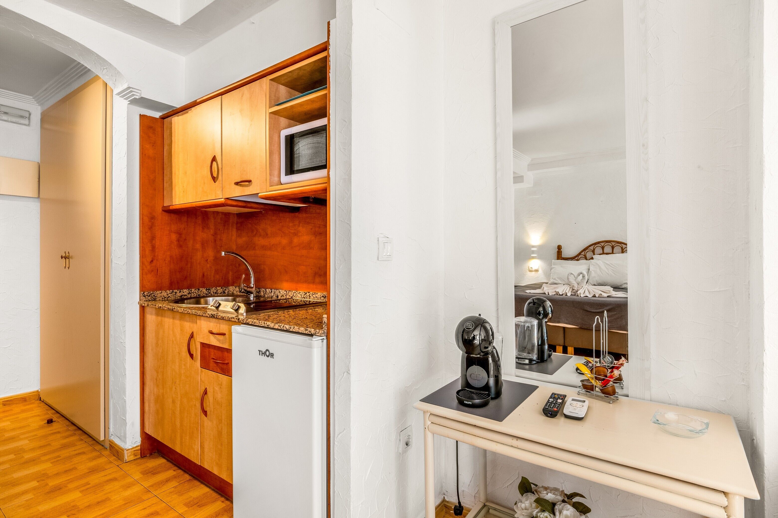 Una cocina compacta con armarios de madera, microondas, refrigerador y una pequeña mesa con cafetera.