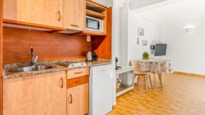 Cocina compacta con armarios de madera, un microondas integrado, un lavabo y un refrigerador pequeño.