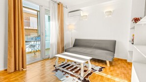 Una sala de estar moderna con un sofá gris, una mesa de centro blanca y un ventanal de vidrio que da a un balcón.