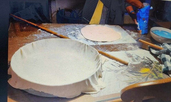 A kitchen with a large round baking surface, a rolling pin, and a bowl of blue liquid.