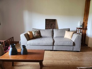 Uma sala de estar com um sofá cinzento, dois vasos, uma mesa de centro de madeira e piso de madeira.