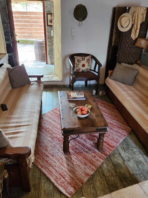 Un salon accueillant avec un canapé, une table basse en bois sur laquelle repose un panier de fruits, un coussin à motifs et un chapeau accroché au mur.