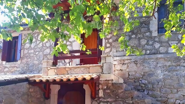 A stone building with a wooden door and a small balcony. - Holiday Home 'Traditional Farmhouse' with Mountain View, Private Terrace and Private Garden (Lefkada)