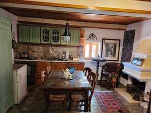 Uma cozinha tradicional com armários verdes, uma mesa de jantar com cadeiras, uma lareira e um tapete estampado.