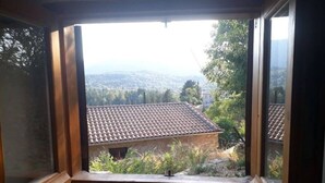 A room with a large window overlooking a residential area with tiled roofs and greenery. - Holiday Home 'Traditional Farmhouse' with Mountain View, Private Terrace and Private Garden (Lefkada)