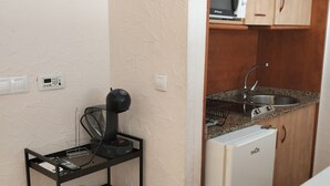 Una cocina compacta con microondas, pileta y heladera pequeña. Hay un carrito metálico negro con una planta y un panel de control.