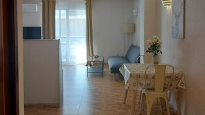 Una sala de estar con sofá, una mesa de comedor con sillas, una lámpara y un cuadro en la pared.