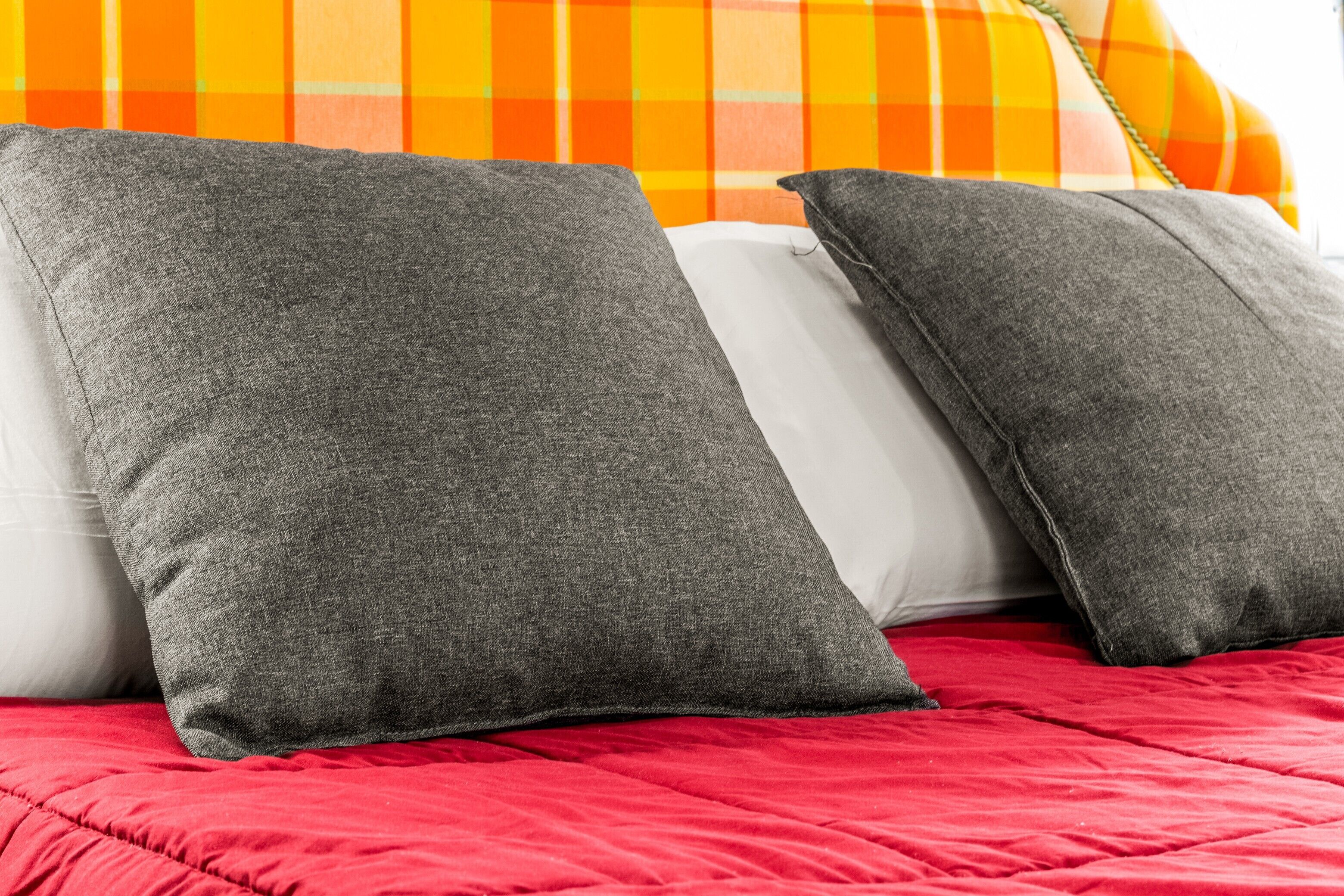Un lit avec des oreillers gris et blancs et une couverture rouge.
