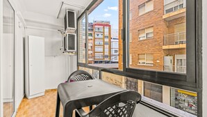 A balcony with a table and chairs, a white door, and a view of a multi-story building.