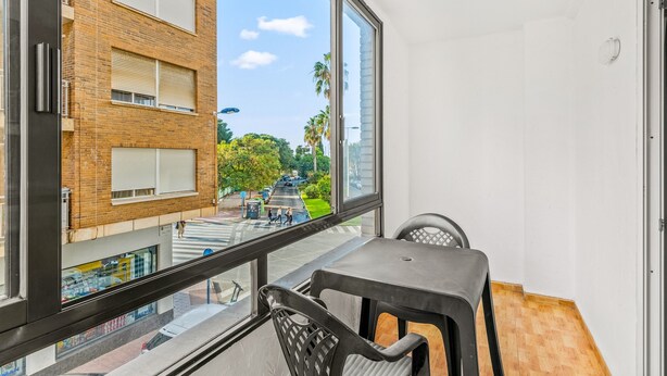 A balcony with a view of a street, a table, and chairs.