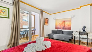 A hotel room with a red bedspread, grey sofa, and a table with a white tablecloth.