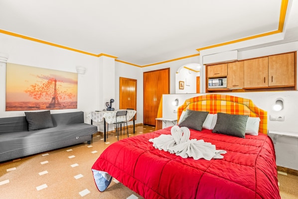 A hotel room with a bed, a sofa, a dining table, and a painting of the Eiffel Tower.