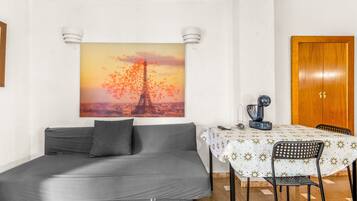 Una habitación con un sofá gris, una mesa de comedor con mantel blanco y un cuadro de la Torre Eiffel.
