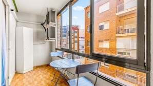 A balcony with a view of adjacent buildings, a white refrigerator, a blue table, and two blue chairs.