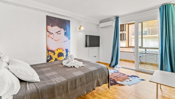 A bedroom with a bed, a flat-screen TV, a painting, and a balcony with a table and chairs.