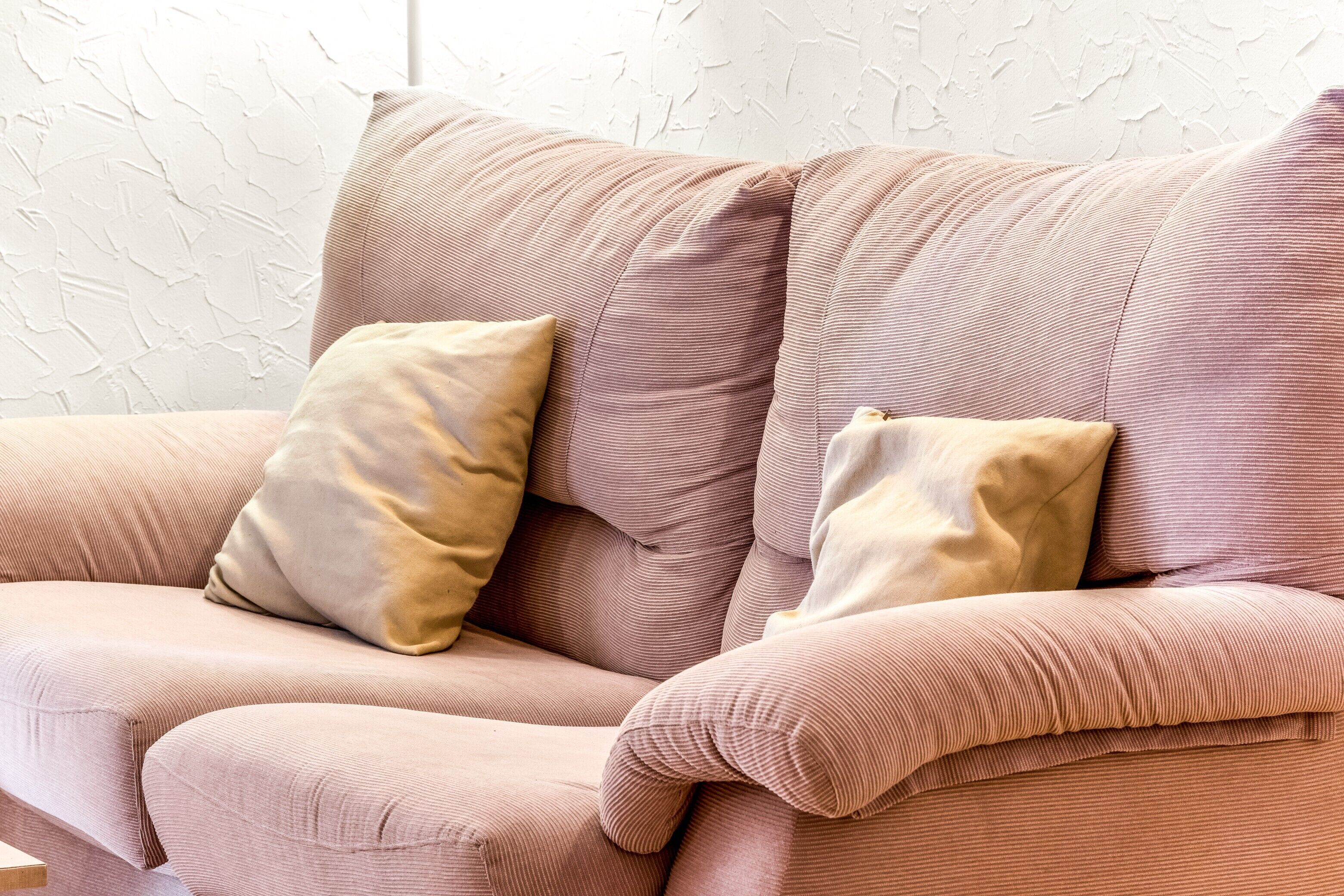 Un sofá color arena con dos almohadas, una pared con textura y un suelo de madera.