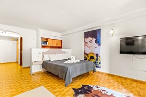 A bedroom with a bed, a TV, a painting, and a wooden floor.