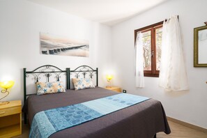 A bedroom with a bed, two bedside tables, a nightstand, a window with curtains, and a wall-mounted picture.
