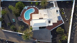 Vista aérea de una propiedad con piscina, un patio cubierto y un edificio grande de color blanco con techo plano.