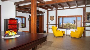 Una habitación con techo de madera, una mesa de comedor con fruta, sillas amarillas y vistas a través de amplios ventanales.
