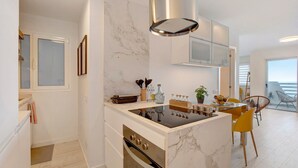 Una cocina moderna con estufa integrada, armarios blancos y una salpicadera de mármol.