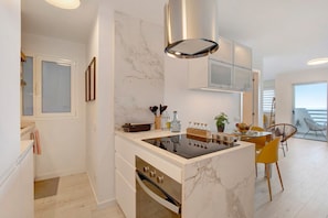 Une cuisine moderne dotée d’une cuisinière intégrée, de meubles blancs et d’un dosseret en marbre.