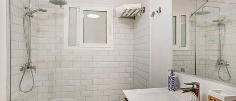 A bathroom with a glass shower enclosure, a white sink, and a mirror.