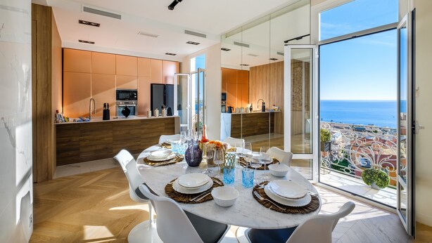 A modern dining area with a large table set for six, a kitchen in the background, and a balcony with a view of the city and sea. - Holiday Apartment 'De luxe Bluesky' with Terrace, Balcony & Wi-Fi (Beausoleil)