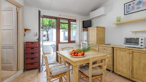 Een keuken met een houten tafel, stoelen, een fruitschaal, een magnetron en een televisie op een plank.