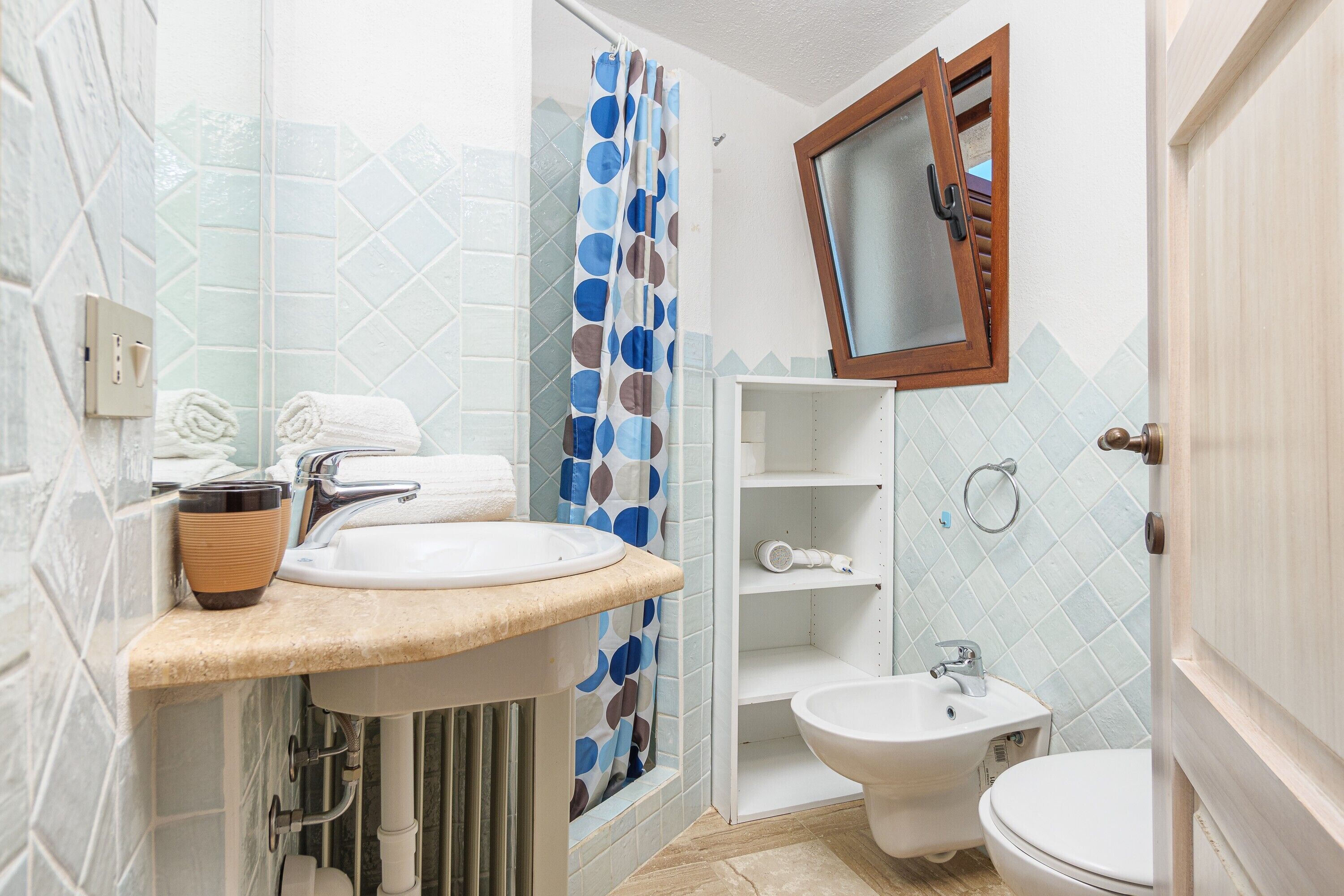 A bathroom with a sink, bidet, and toilet, a shower curtain, and a mirror.