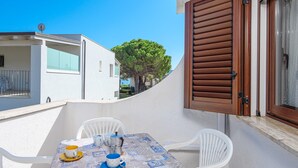 Een balkon met een tafel voor twee personen, witte stoelen en een tafelkleed met een nautisch thema.