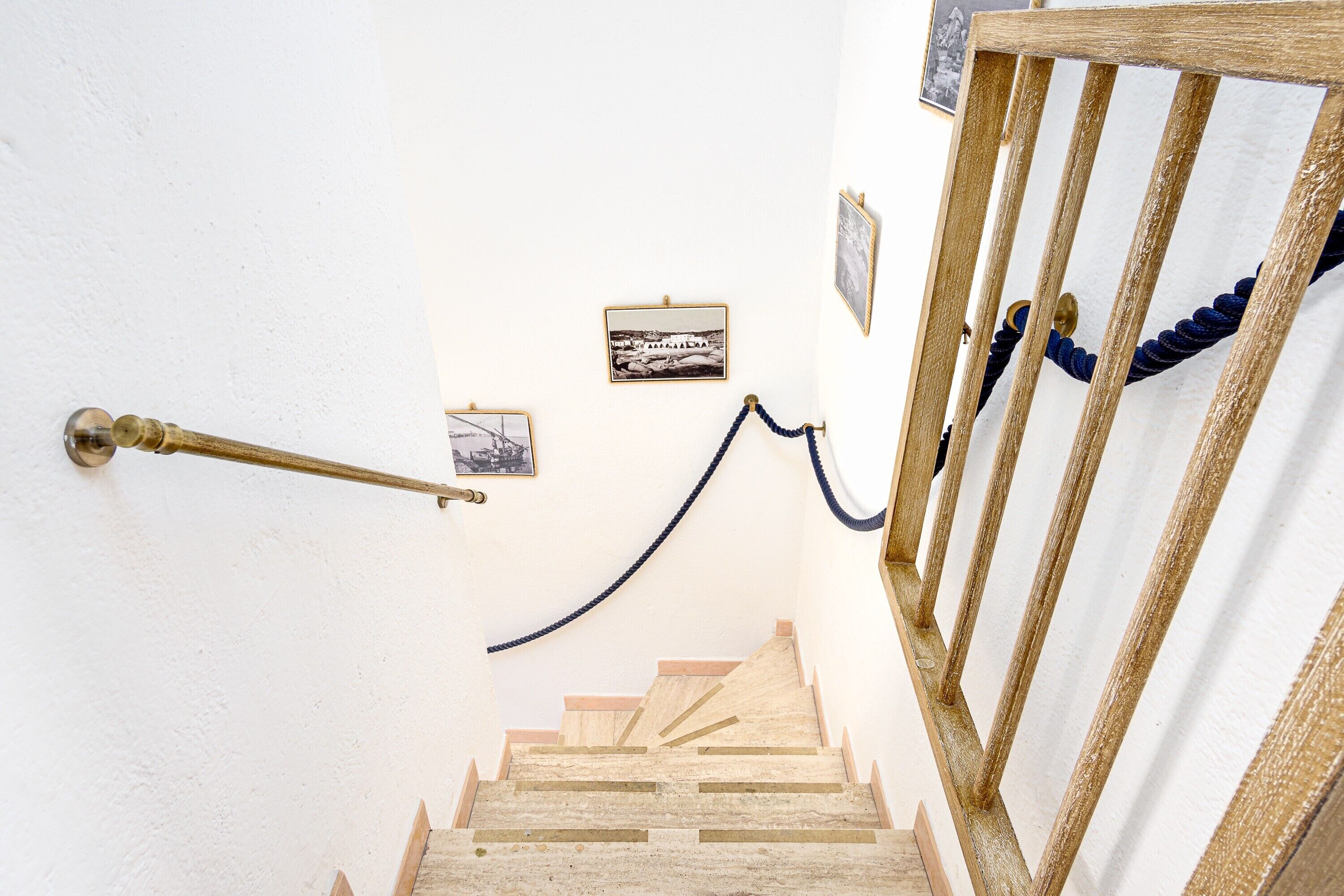 A wooden staircase with a handrail, a rope barrier, and framed pictures on the wall.