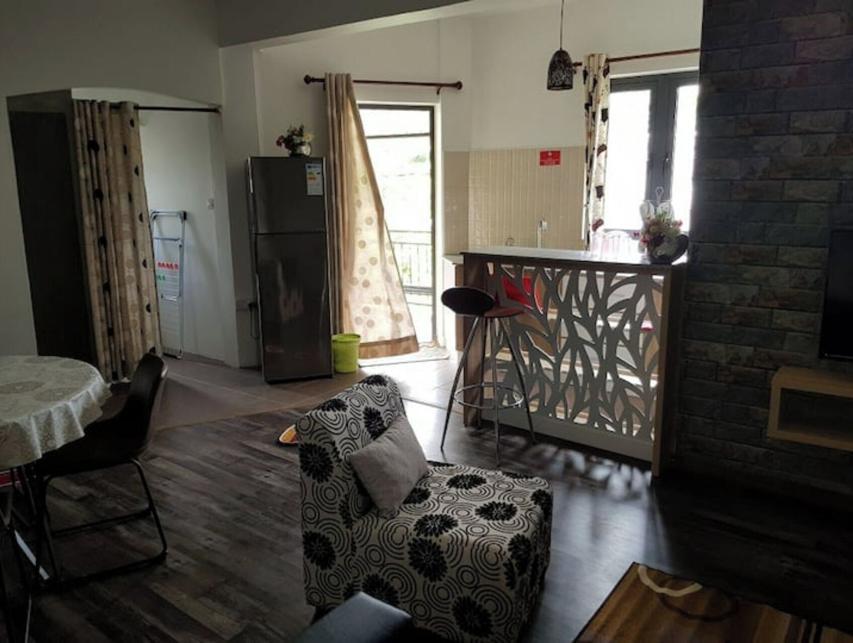 Un espace de vie compact comprenant un coin cuisine, un espace repas avec une table et des chaises, et un pouf à motifs.