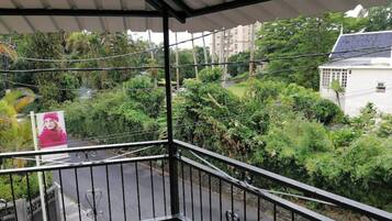 Un balcon donnant sur un jardin luxuriant et des immeubles d’habitation.