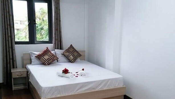 Un dormitorio con cama, mesita de noche, ventana con cortinas y vistas al exterior.