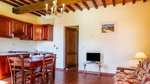 A kitchen with wooden cabinets, a dining table with chairs, a TV on a stand, and a sofa in a living area. - Apartment 'Grillo' with Shared Pool, Wi-Fi and Air Conditioning (Montiano)
