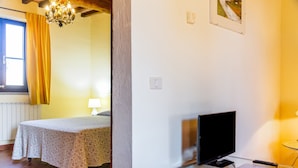 A room with a bed, a television on a glass table, a window with curtains, and a chandelier. - Apartment 'Grillo' with Shared Pool, Wi-Fi and Air Conditioning (Montiano)