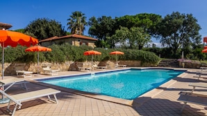A swimming pool with lounge chairs and umbrellas, surrounded by greenery and a stone building. - Apartment 'Grillo' with Shared Pool, Wi-Fi and Air Conditioning (Montiano)