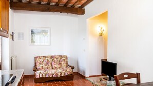 A room with a sofa, a dining table, a TV, and a wall-mounted light fixture. - Apartment 'Riccio' with Shared Pool, Wi-Fi and Air Conditioning (Montiano)