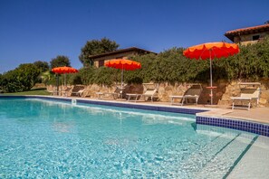 A swimming pool with clear blue water, surrounded by lounge chairs and red umbrellas, with a stone wall and a building in the background. - Apartment 'Farfalla' with Shared Pool, Wi-Fi and Air Conditioning (Montiano)