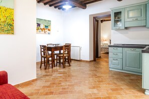 A dining area with a table and chairs, a kitchen with cabinets, and a radiator on the floor.