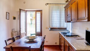 A kitchen with wooden cabinets, a dining table with chairs, a window with curtains, and a radiator. - Apartment 'Formica' with Shared Pool, Wi-Fi and Air Conditioning (Montiano)