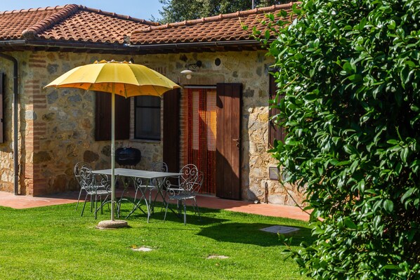 Un edificio de piedra con techo de tejas, un patio con mesa y sillas, y un paraguas amarillo.