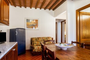 Una cocina con refrigerador, armarios de madera, una mesa de comedor con sillas y un sofá.