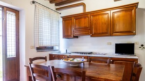 A kitchen with wooden cabinets, a dining table with chairs, a bowl on the table, and a window with a curtain. - Apartment 'Formica' with Shared Pool, Wi-Fi and Air Conditioning (Montiano)