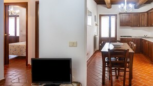 Une pièce comprenant un lit, un bureau avec un ordinateur, une table à manger avec des chaises, et un coin cuisine avec des meubles en bois et un lustre.