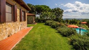 Un bâtiment en pierre doté d’une terrasse carrelée, d’une pelouse bien entretenue et d’une piscine agrémentée de parasols.