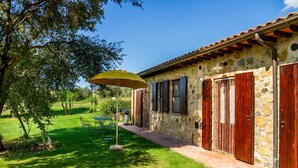 Un bâtiment en pierre avec un toit en tuiles, une terrasse avec des chaises et une table, et un grand parasol.